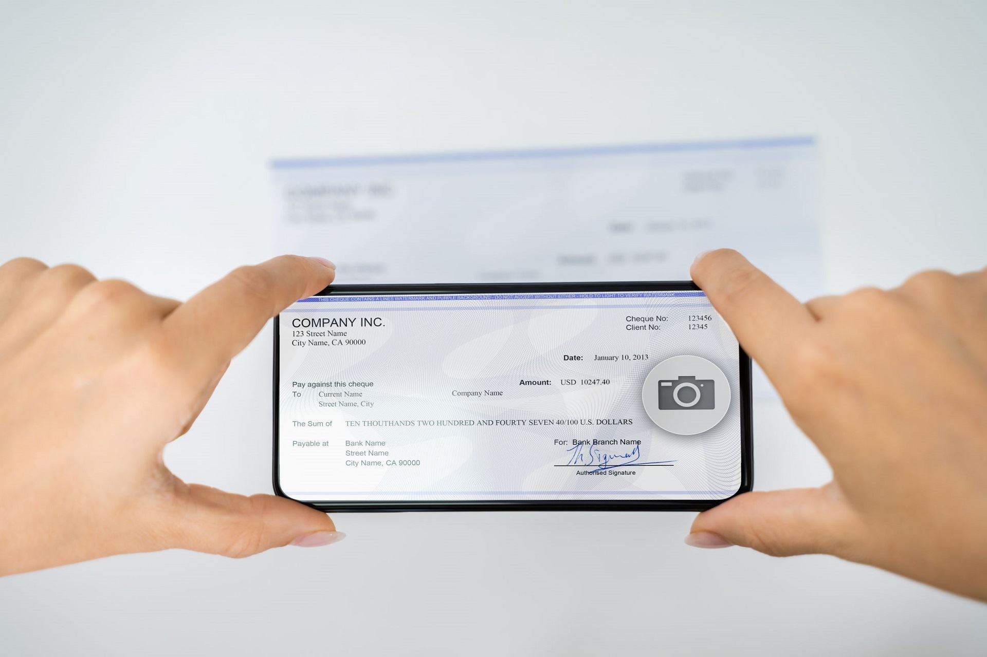 Hands holding a cell phone while taking a picture of a paper check