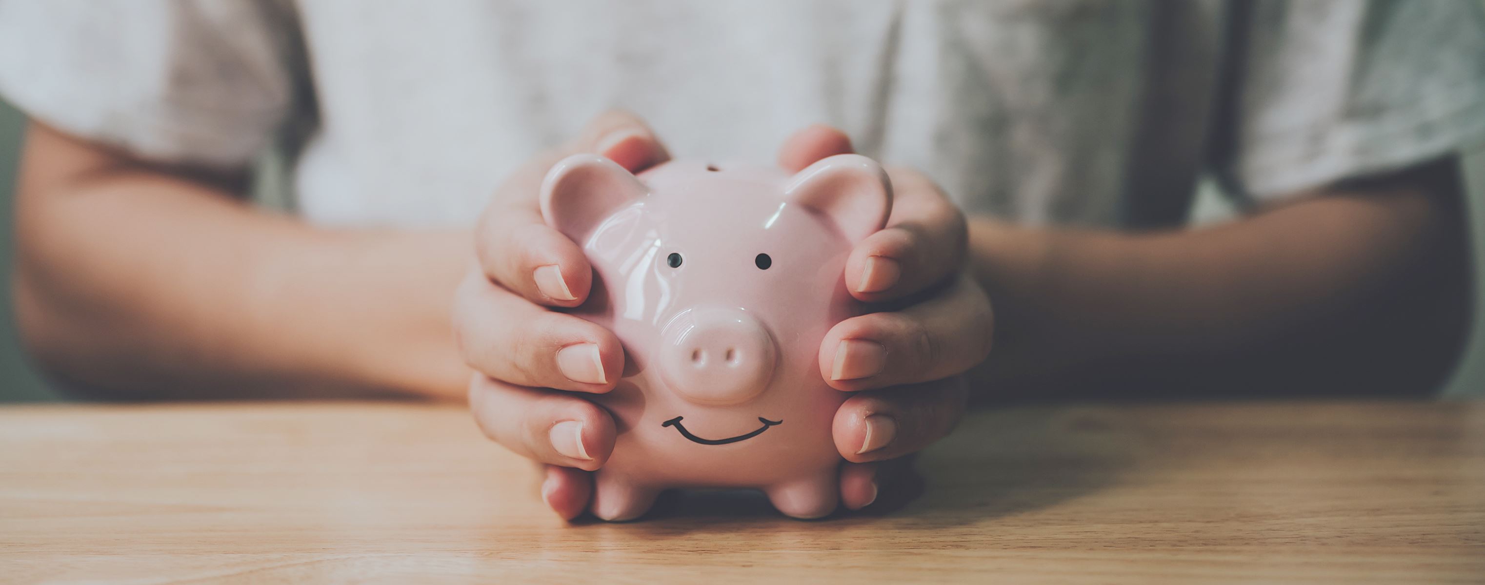 Womans hands holding a pink smiling piggy bank 