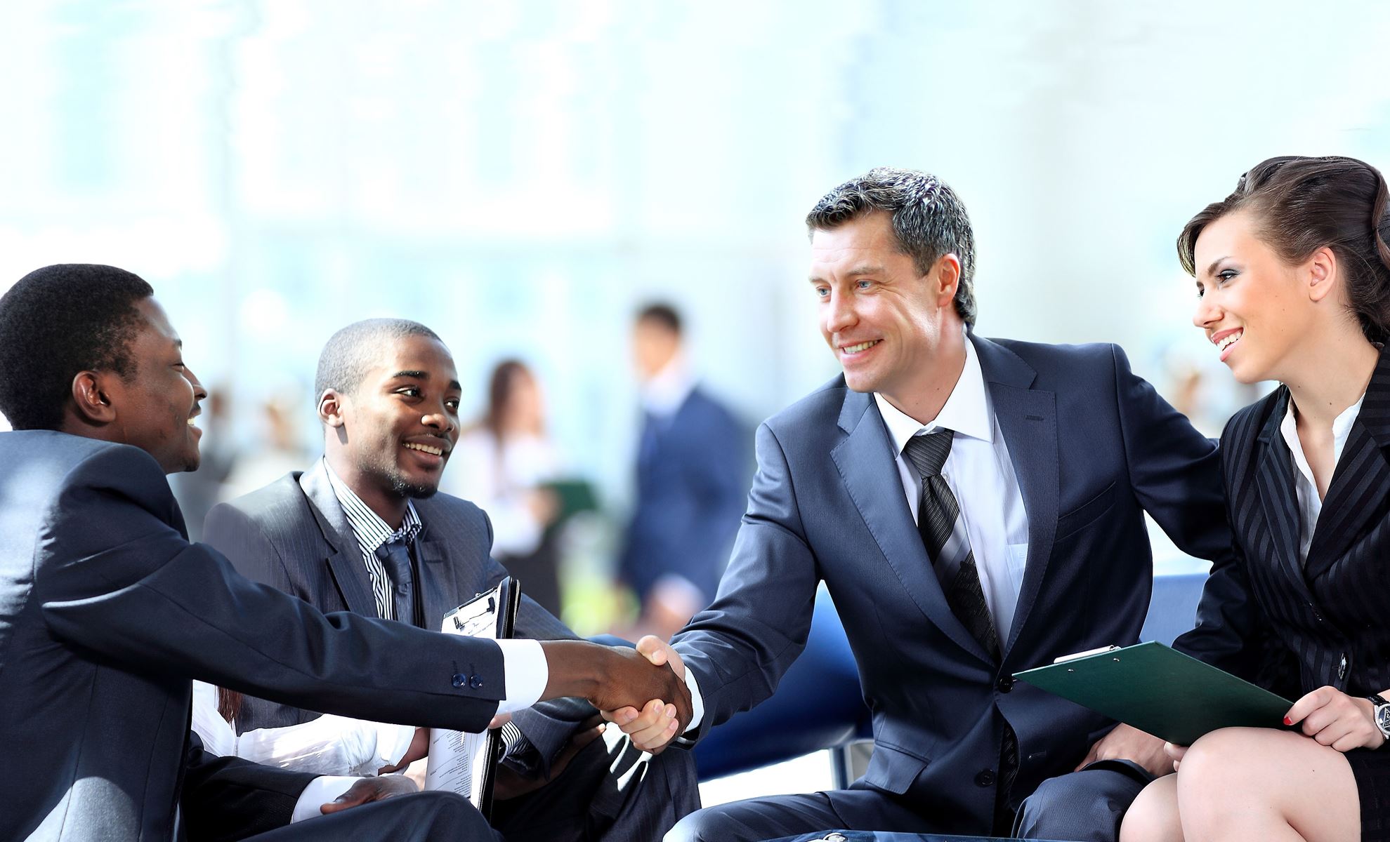 Two men shaking hands and smiling, there is another man and woman watching and smiling