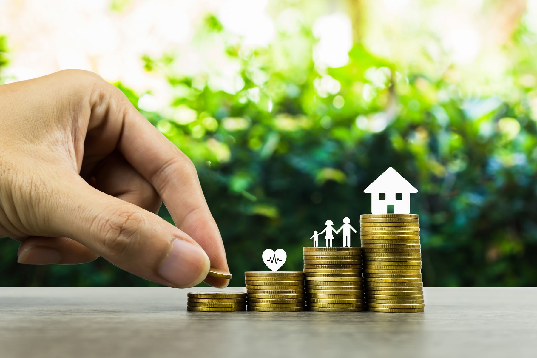 Hand stacking coins like a graph with a heart on one stack, a cutout of a family on one stack and a home on the last stack